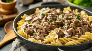 Creamy beef stroganoff mixed with egg noodles in a serving bowl, garnished with parsley, ready for plating.